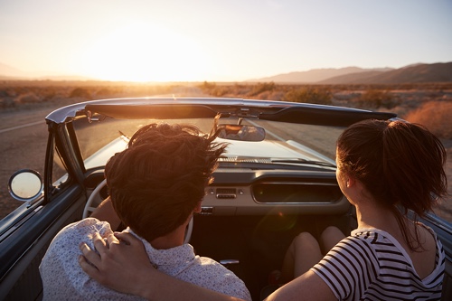 Fall Car Care with John's Auto Pros in Escondido, CA; image of young couple with arms around each other while driving their convertible car in the California desert during sunset