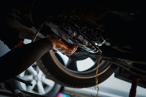 When to Flush a Transmission and Why It Is Important. Transmission flush in Escondido, CA by John’s Auto Pros. Image of a car mechanic draining the old automatic transmission fluid (ATF) under a car.
