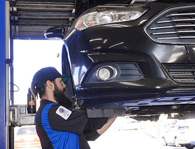 Brake service and repair in Escondido, CA with John's Auto Pros; image of ASE certified master tech performing brake maintenance on car on lift in shop bay