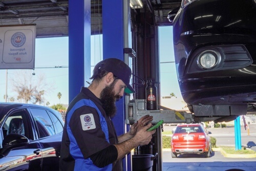 Brake service and repair in Escondido, CA with John's Auto Pros; image of ASE certified tech checking over diagnostic tool while performing inspection on brakes of car on lift in shop bay area