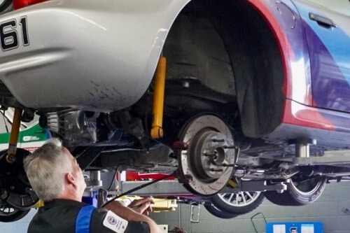 Brake service and repair in Escondido, CA with John's Auto Pros; image of ASE certified tech working on brakes while building track car in shop bay area