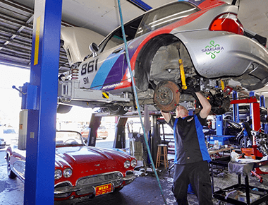 Suspension service and repair at John's Auto Pros in Escondido, CA image of our tech underneath car on lift rebuilding suspension system of race car