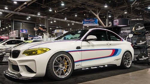 4 BMW Performance Upgrades in Escondido, CA by John's Auto Pros. Image of a white, customized BMW M2 car at an auo trade show.