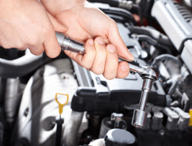 An auto repair technician holding a wrench under the hood of a car at John's Auto Pros in Escondido, California