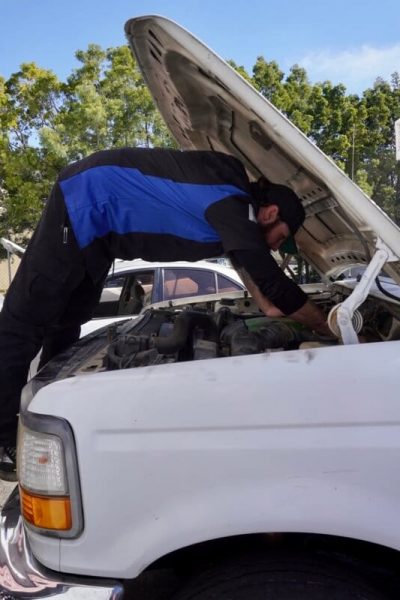 Engine Rebuild and Restoration services in Escondido, CA with John's Auto Pros; close up image of ASE certified master tech climbing up on truck engine to diagnose